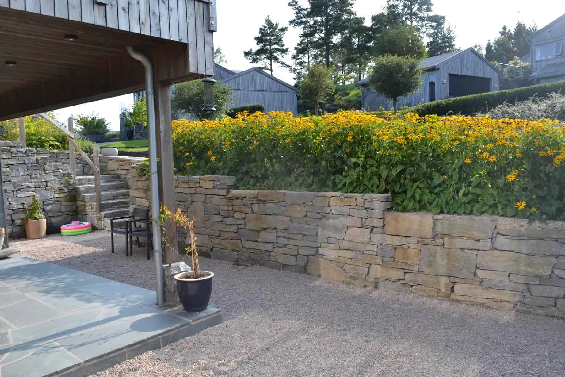Terrasse med naturstein og blomsterbed med gule blomster
