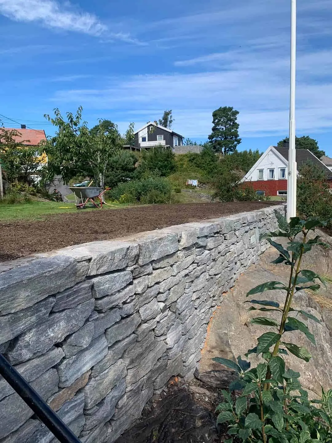 Steinmur med opparbeidet hage og bolighus i bakgrunnen