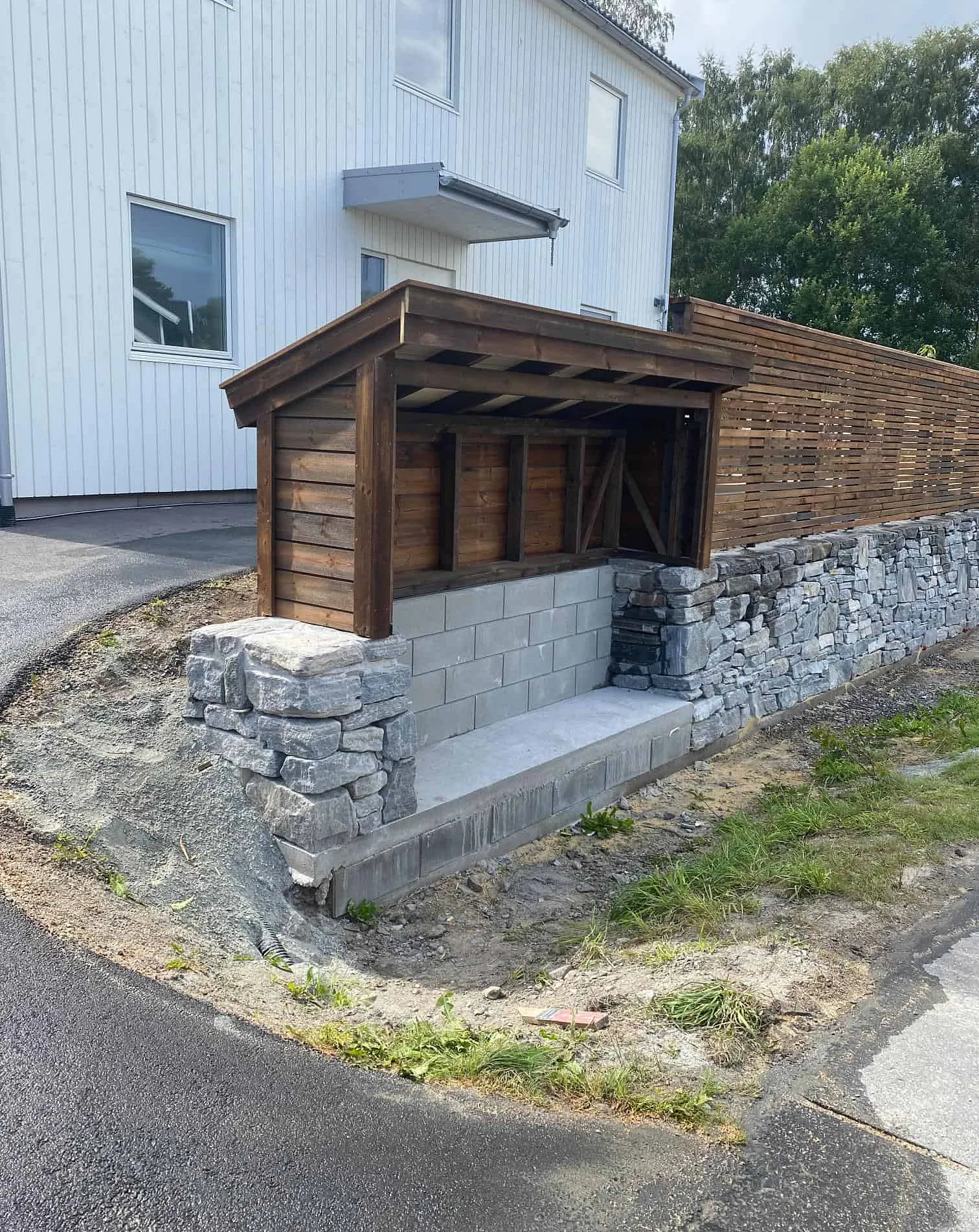 Lite skur med steinmur og trepanel foran en hvit bygning