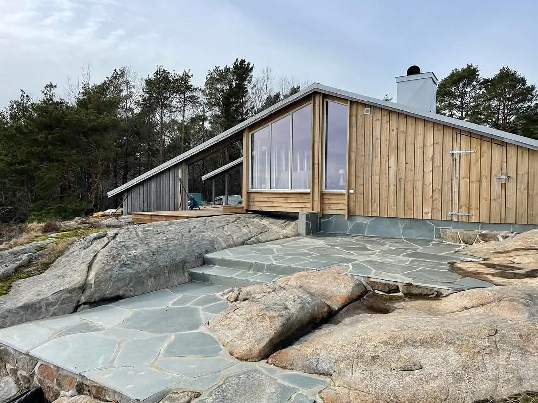 Hytte i tre med store vinduer, skifer og svaberg rundt