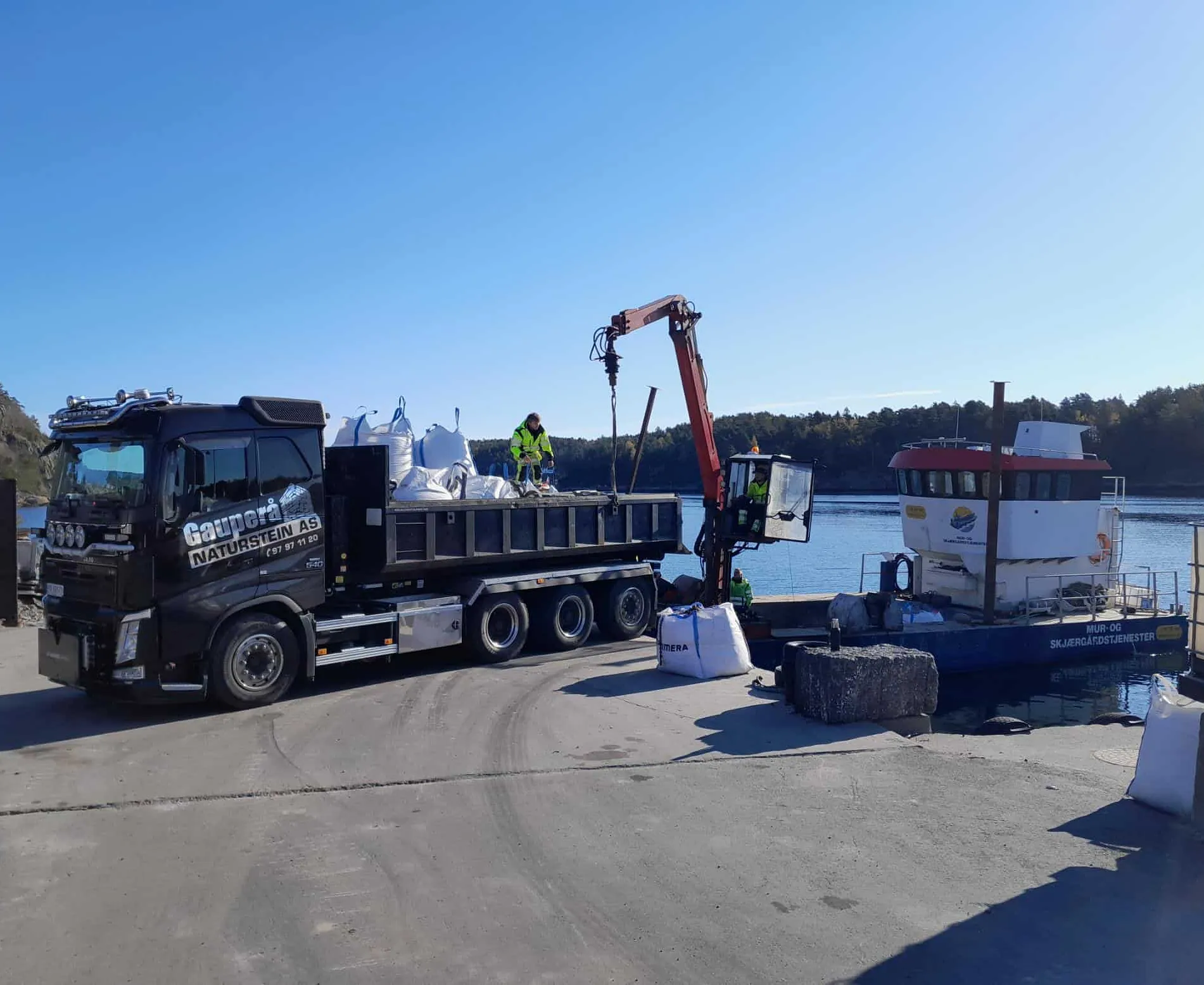Lastebil og kran lossing av materialer ved kai med arbeidsbåt