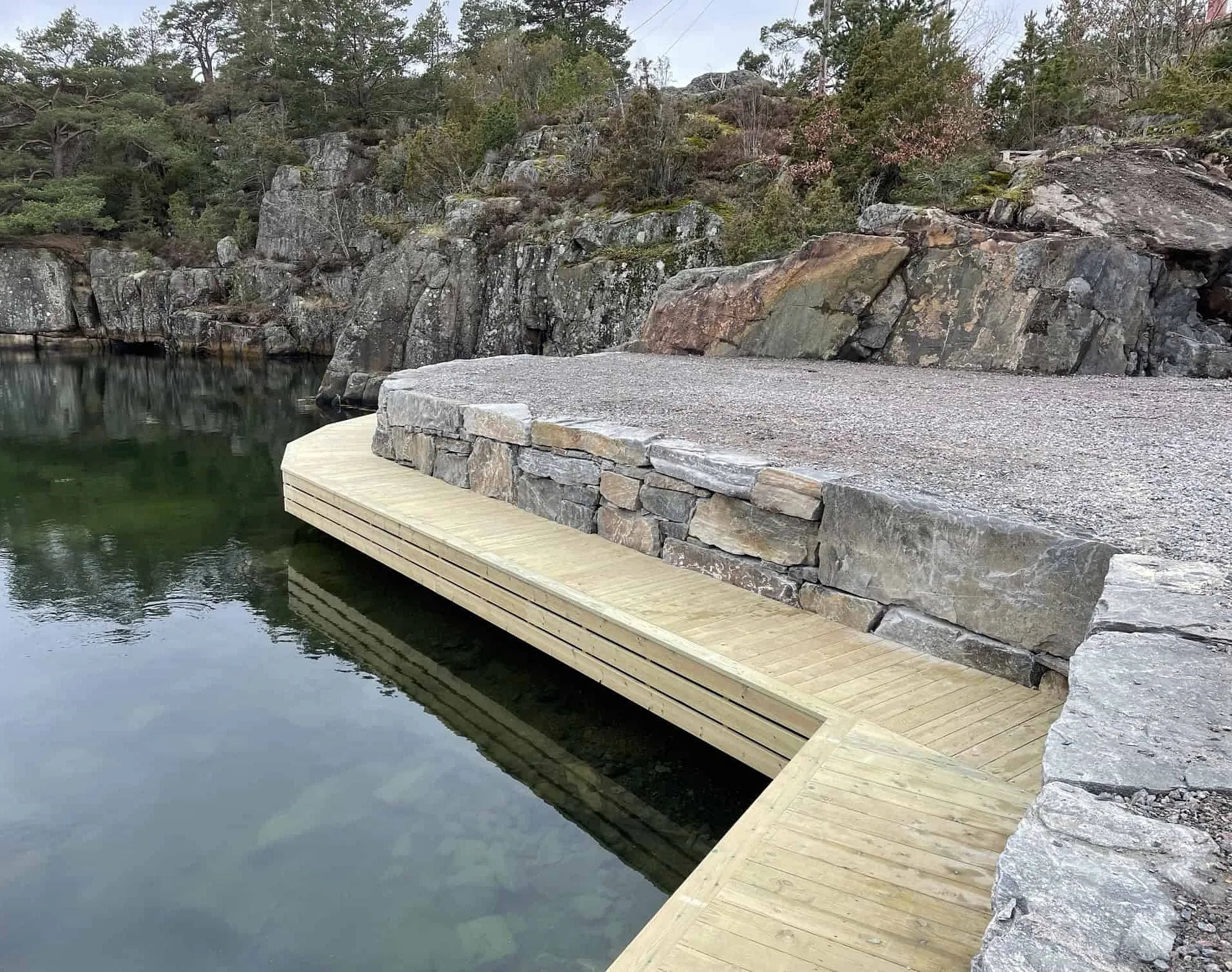 Brygge i stein og tre ved vannet omgitt av klipper